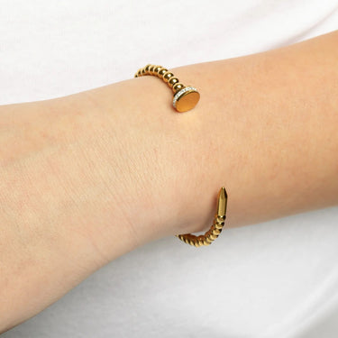 Gold bracelet on a wrist with a plain background