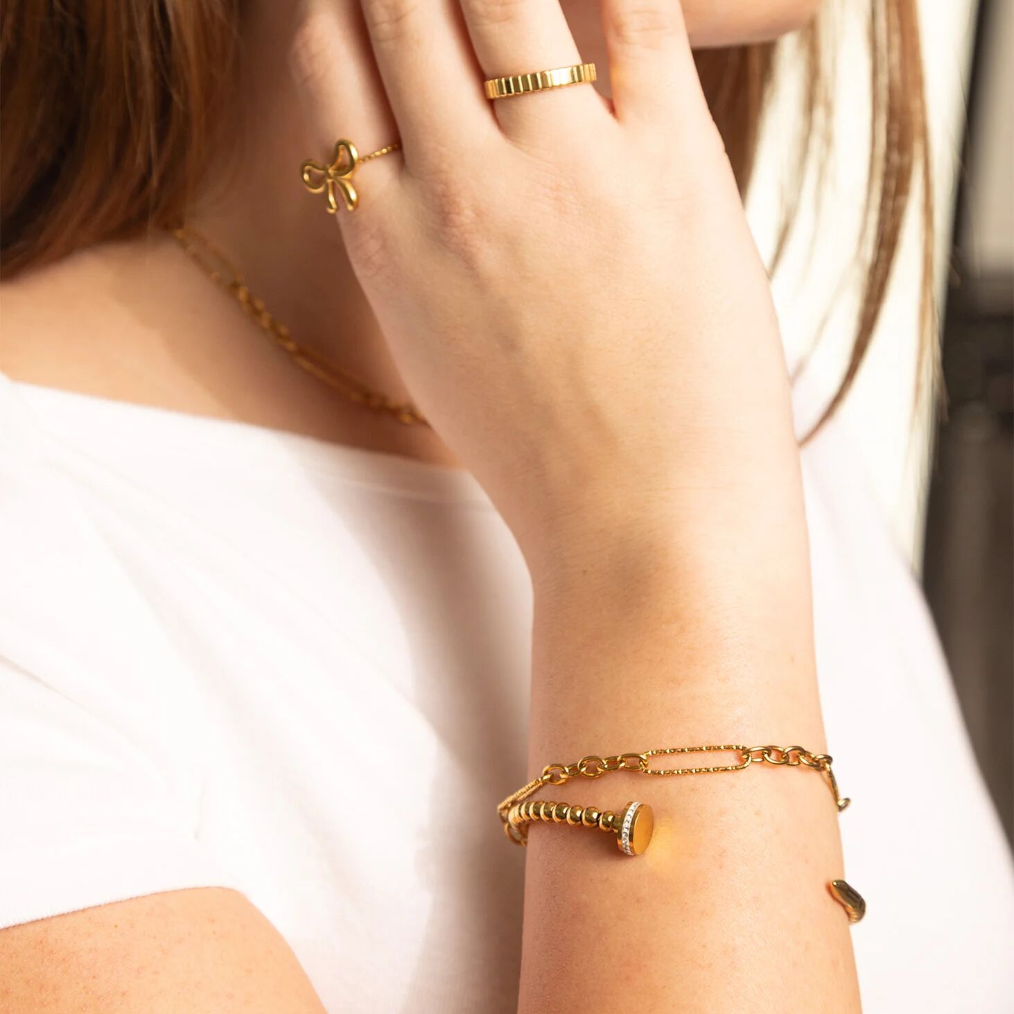 Close-up of a person wearing gold jewelry including a bracelet, ring, and necklace.
