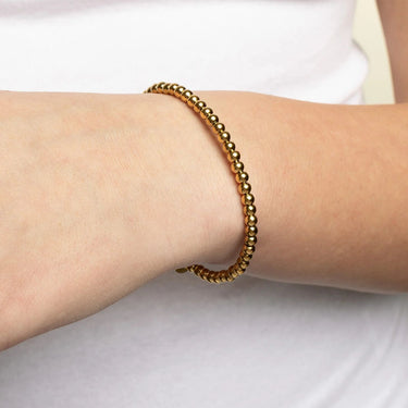 Gold beaded bracelet on a wrist against a white background