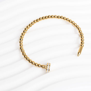 Gold beaded bracelet with a pen on a white background