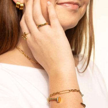 Close-up of a person wearing gold jewelry including earrings, ring, and bracelet.