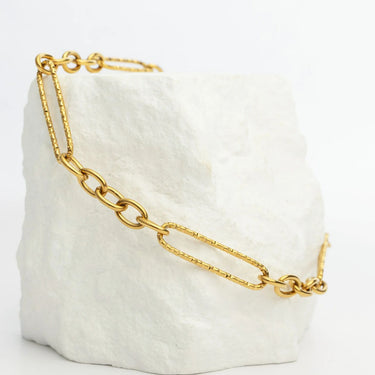 Gold chain bracelet on a white textured surface