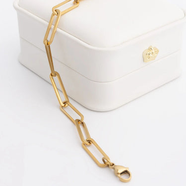 Gold chain necklace on a white surface with a white box in the background