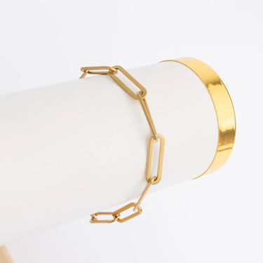 Gold bracelet on a white cylindrical stand with a white background