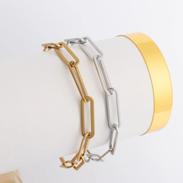 Two gold and silver bracelets on a white surface with a yellow cylindrical object.