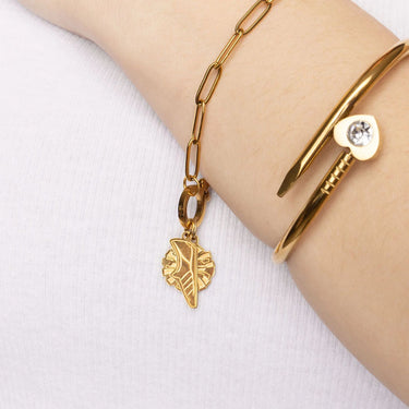 Gold bracelet with leaf charm on a wrist against a white background