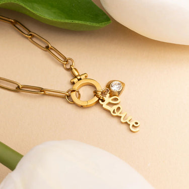 Gold chain necklace with a 'love' charm on a beige background