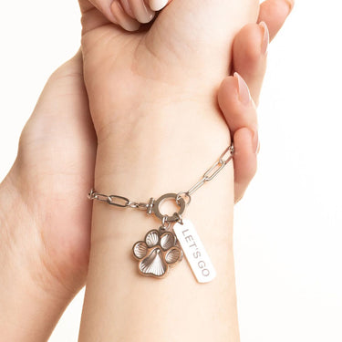 Silver bracelet with paw charm and 'LET'S GO' tag on wrist against a white background