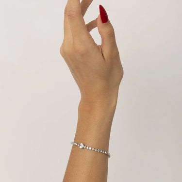 Hand wearing a silver bracelet on a plain background