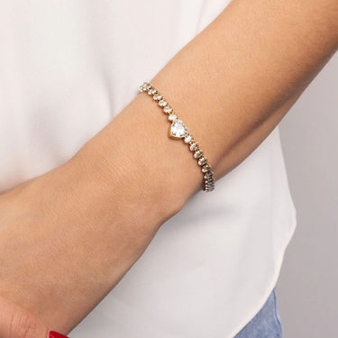 Bracelet with heart-shaped charm on a wrist against a neutral background
