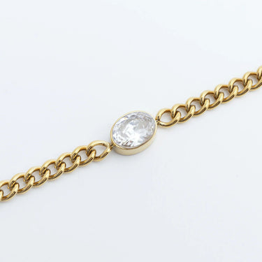 Gold chain bracelet with a clear gemstone on a light gray background