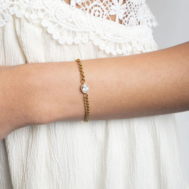 Gold bracelet with a pearl on a wrist against a white lace background