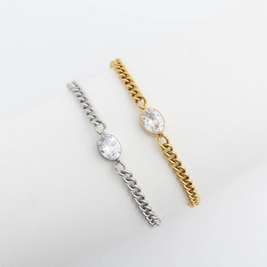 Two chain earrings, one silver and one gold, with clear gemstones on a light gray background.