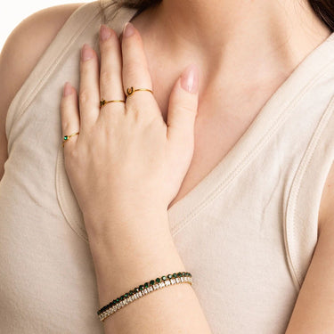 Close-up of a hand wearing gold rings and a bracelet on a neutral background