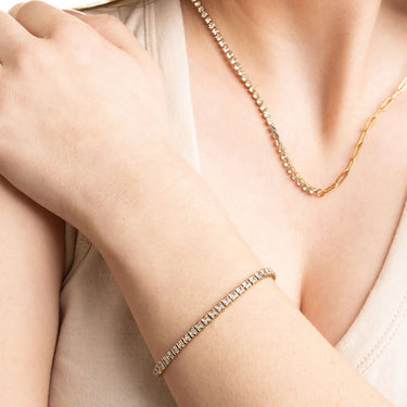 Gold bracelet and necklace on a person's wrist and neck against a neutral background