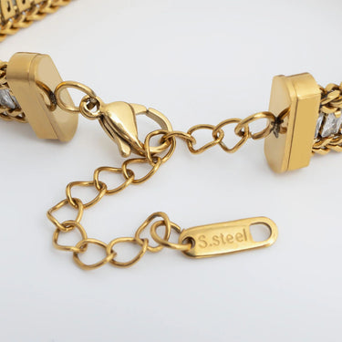 Gold bracelet with heart-shaped links and a tag on a white background