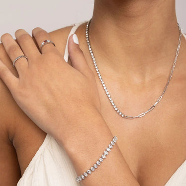 Silver necklace, bracelet, and ring on a person's hand and arm against a neutral background