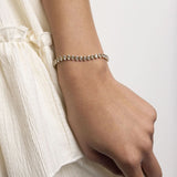 Close-up of a hand wearing a delicate bracelet on a plain background