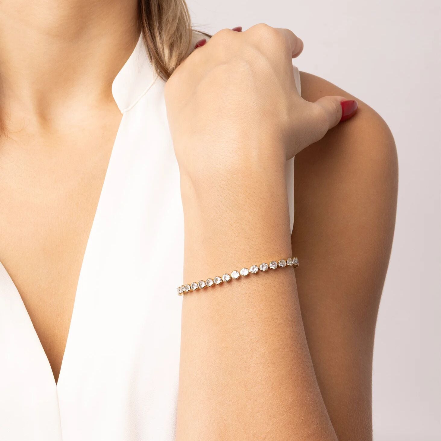 Close-up of a woman's arm wearing a diamond bracelet on a plain background