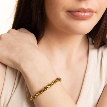 Gold bracelet on a person's wrist with a neutral background