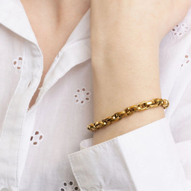 Gold bracelet on a person's wrist with a white blouse in the background