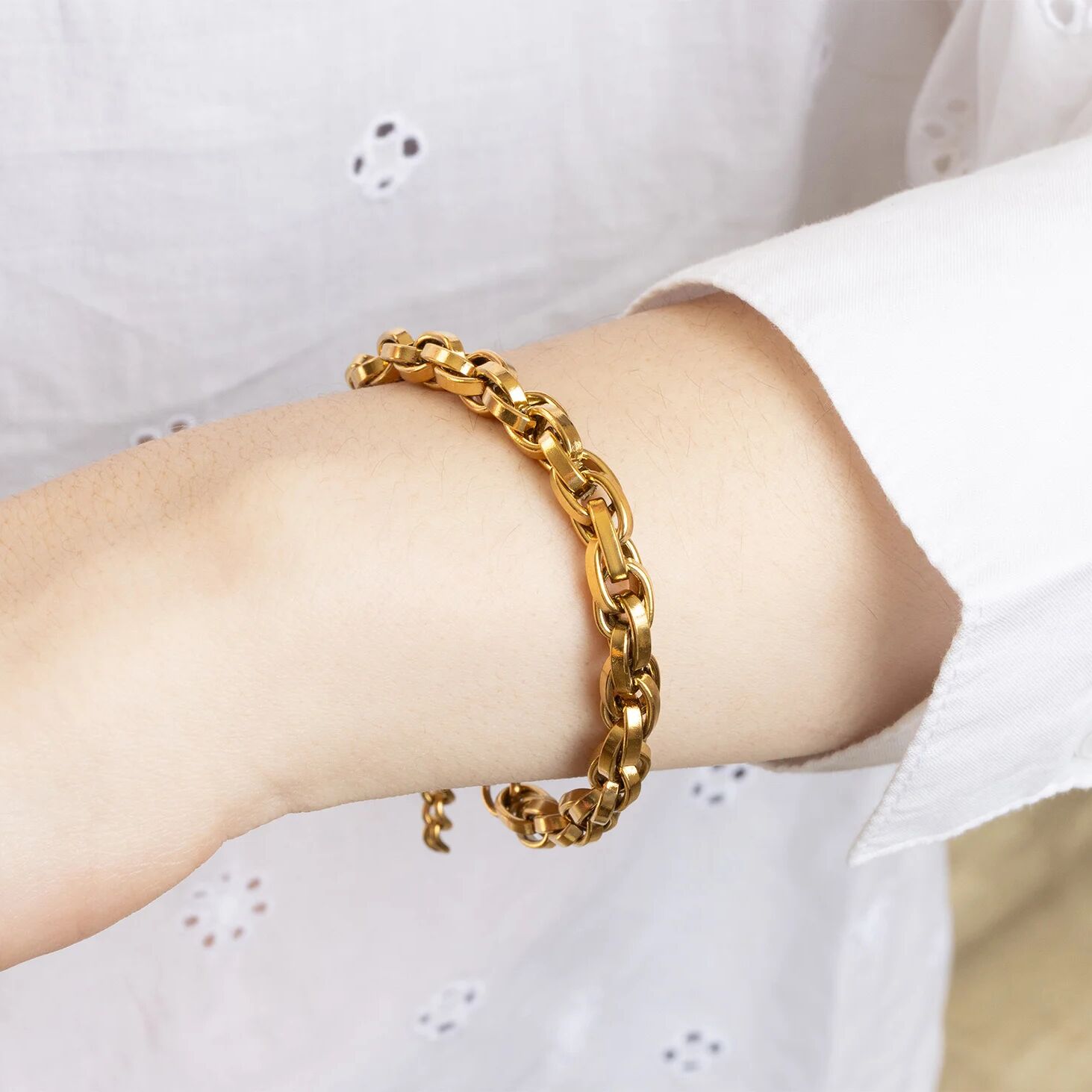Gold chain bracelet on a wrist with a white shirt background
