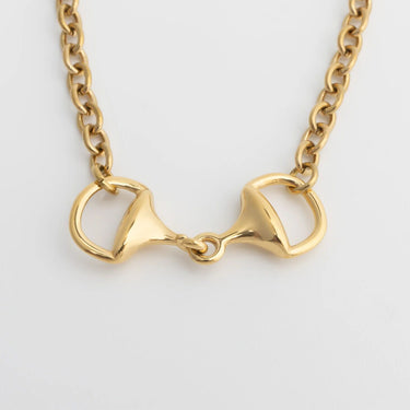 Gold bracelet with a horse bit pendant on a light gray background