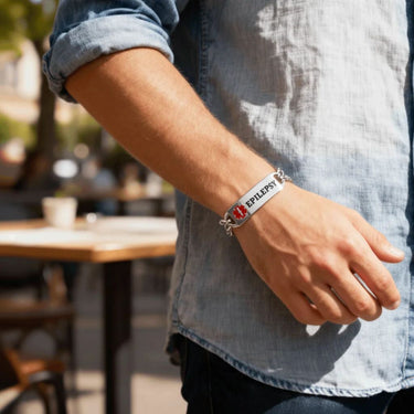 Person wearing a silver bracelet with 'Epilepsy' on it, standing outdoors.