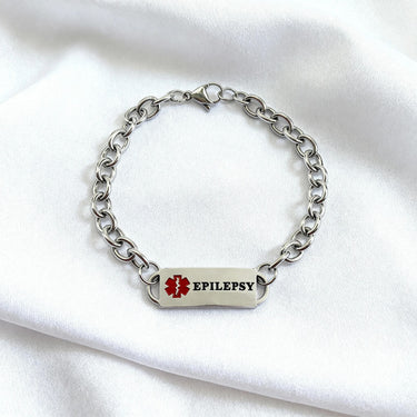 Silver chain bracelet with a medical alert tag on a white fabric background