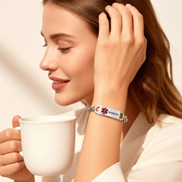 Woman holding a white mug wearing a silver bracelet with a medical alert tag.