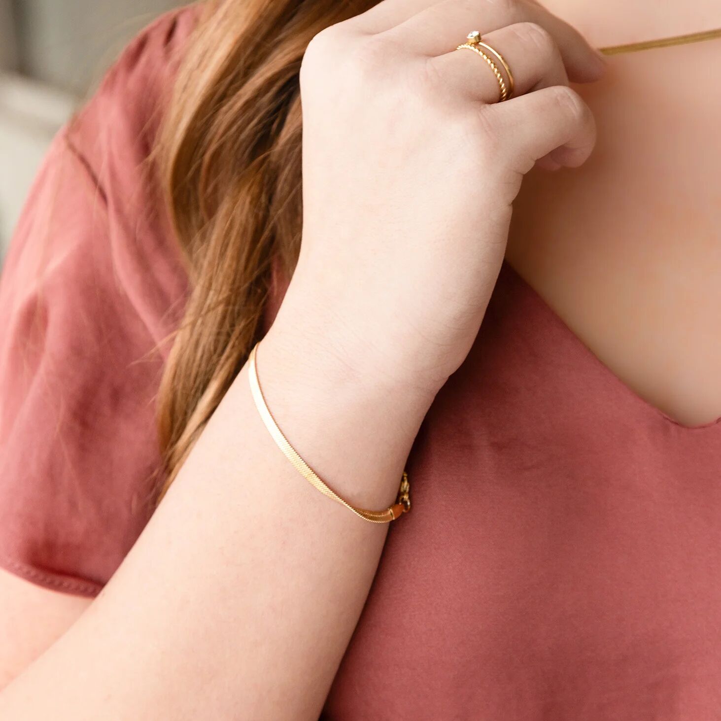 Person wearing gold jewelry including a ring and bracelet on a plain background
