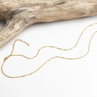 Gold Singapore Belly Chain on a white surface with a piece of driftwood.