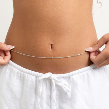 Person wearing white pants with a silver Satellite Belly Chain around the waist on a plain background