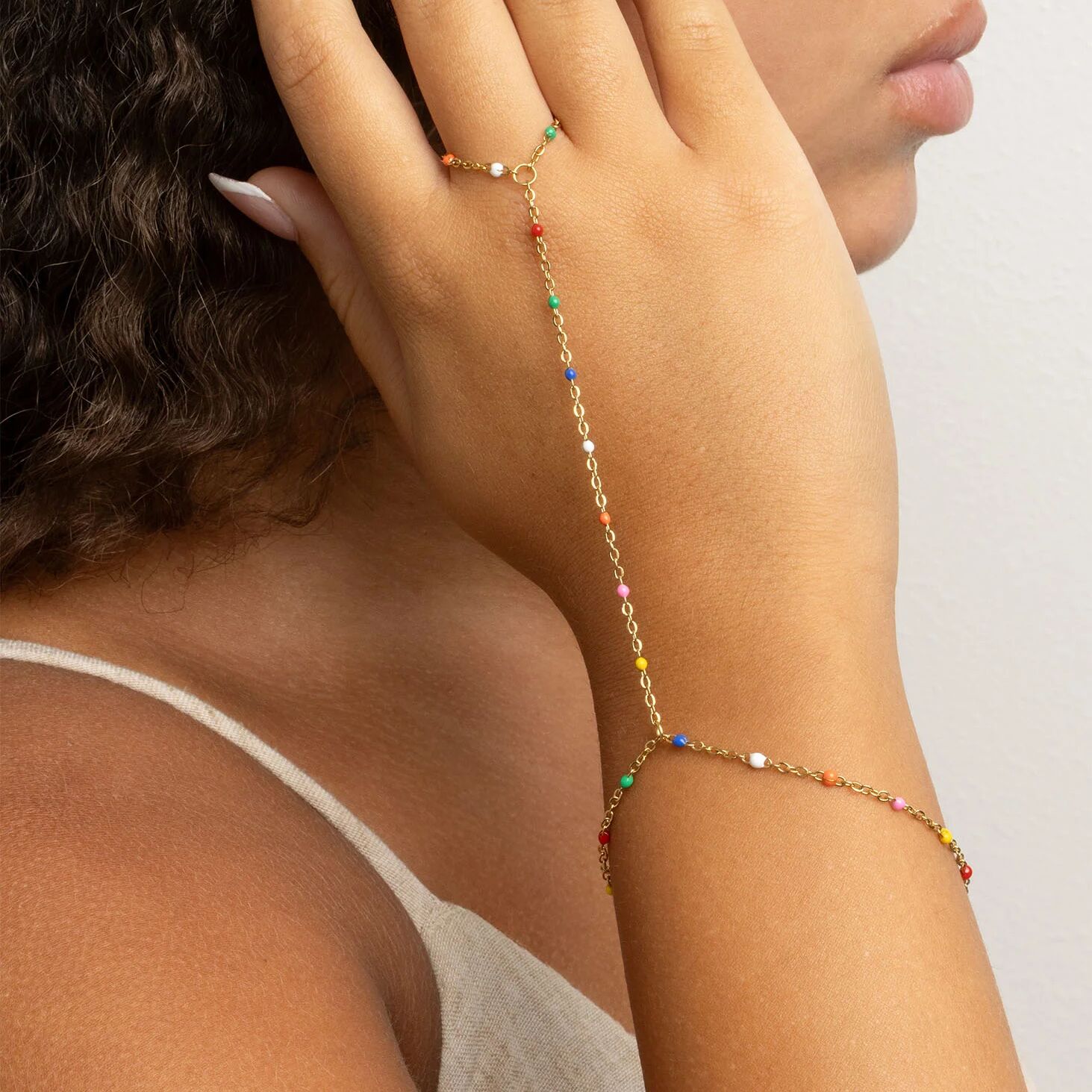 Close-up of a person wearing a gold Multi Color Hand Chain on a plain background