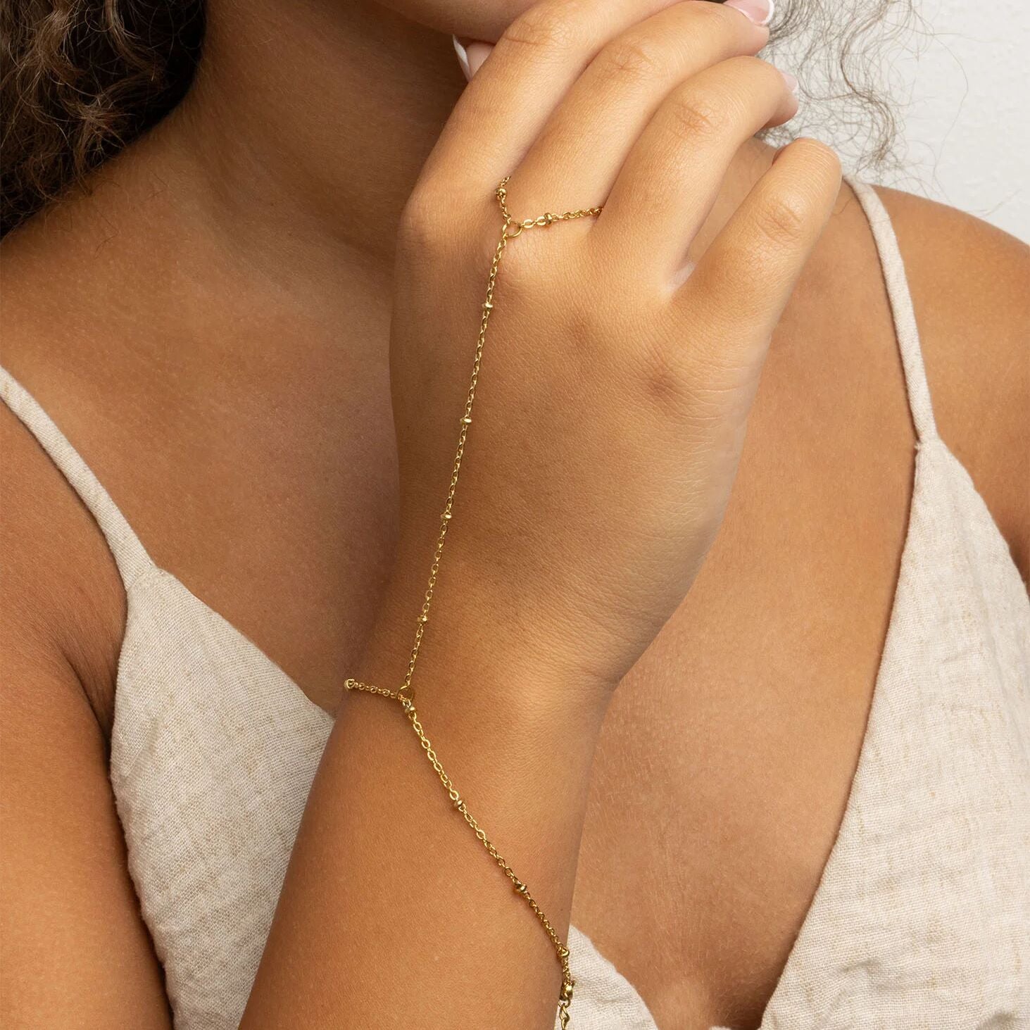 Gold Satellite Hand Chain  on a wrist with a neutral background