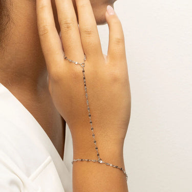Hand wearing a delicate silver Lip Hand Chain on a plain background