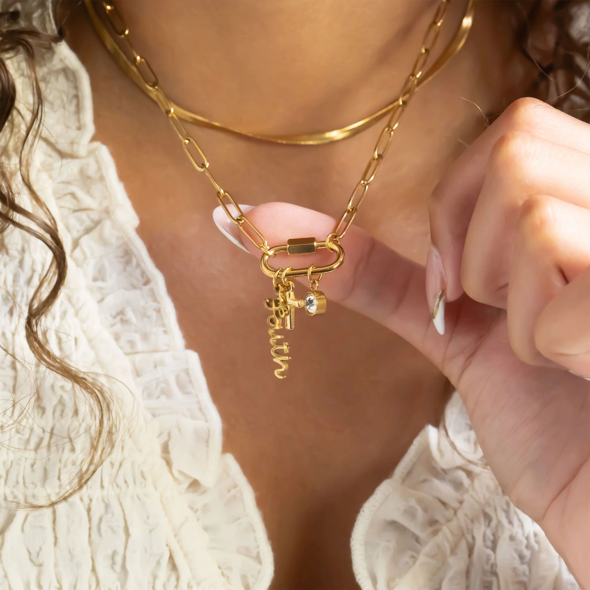 Close-up of a gold chain necklace with a clasp and small charm worn by a person.