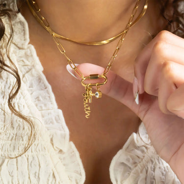 Close-up of a gold chain necklace with a clasp and small charm worn by a person.