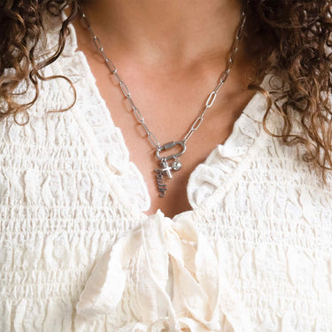 Close-up of a person wearing a silver chain necklace with charms against a white textured fabric background.