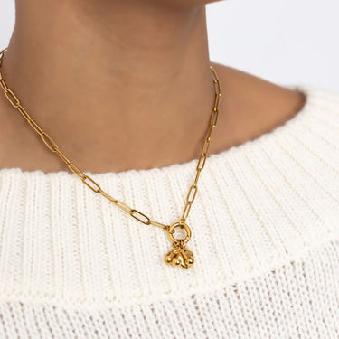 Gold chain carabiner necklace with small charms on a white sweater