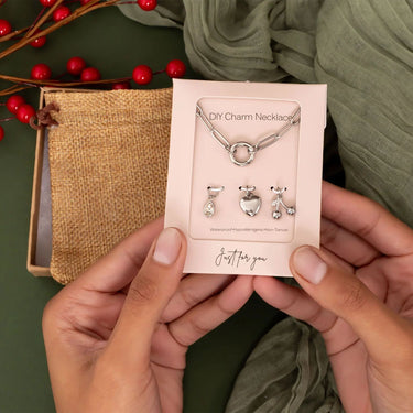 DIY charm necklace set in packaging held by hands with a green background