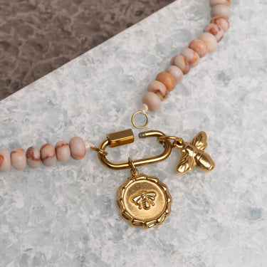 Necklace with gold bee charm and pink beads on a marble surface