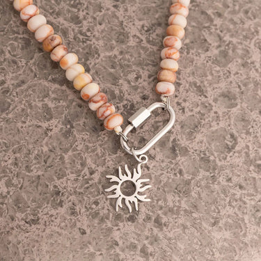 Necklace with sun charm and beaded chain on a textured surface