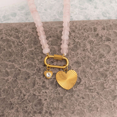 Necklace with pink beads and gold heart pendant on a textured surface