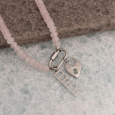 Necklace with pink beads and 'mini' charm on a stone surface
