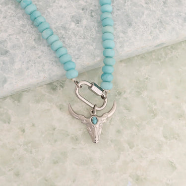 Necklace with turquoise beads and silver bull head charm on a marble surface