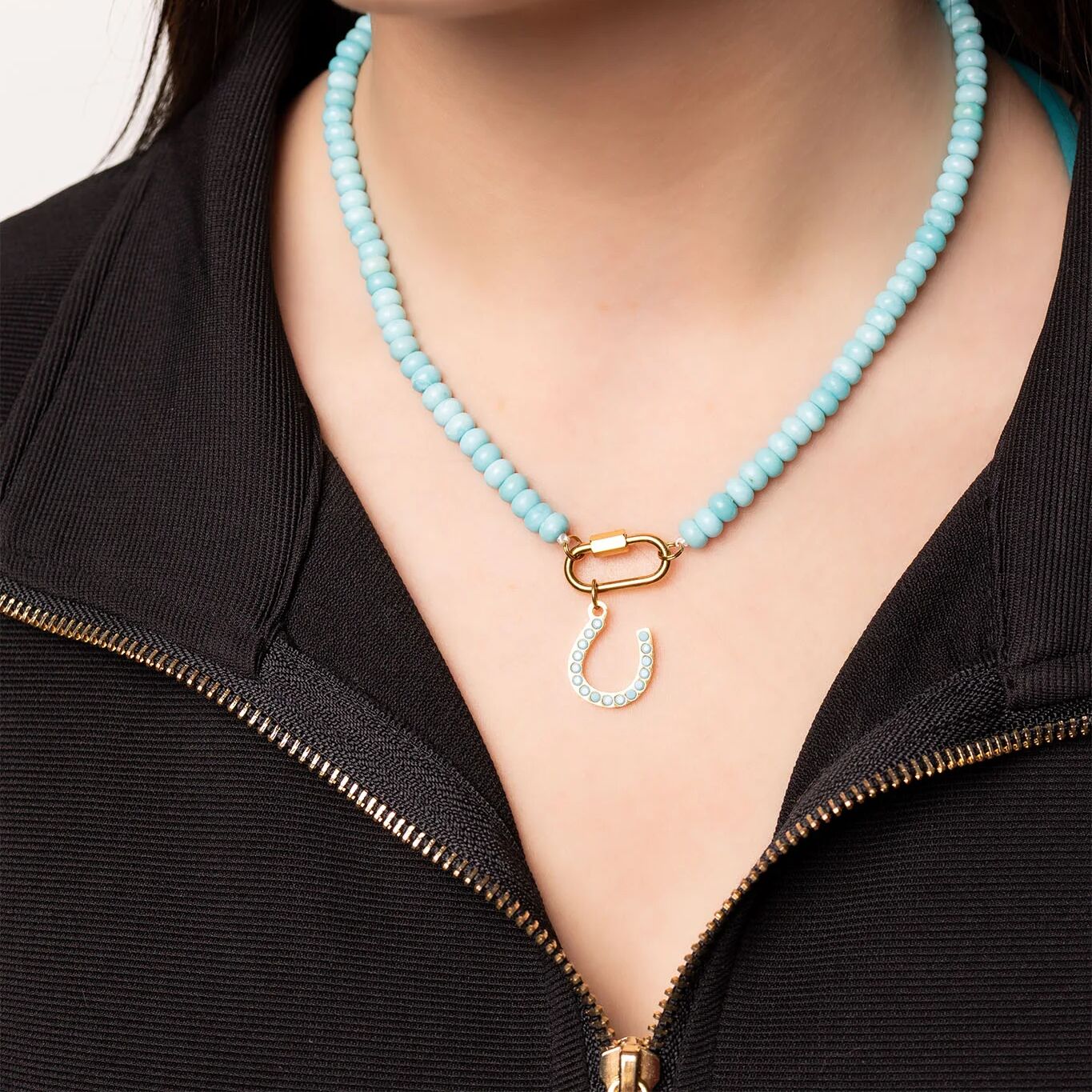 Turquoise beaded necklace with a gold clasp worn by a person in a black jacket.