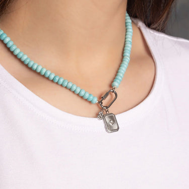 Turquoise beaded necklace with a silver clasp worn by a person on a plain background