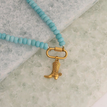 Turquoise beaded necklace with a gold cowboy boot charm on a marble surface