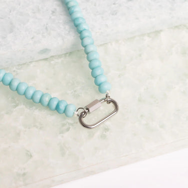 Light blue beaded necklace with a metal clasp on a light marble background